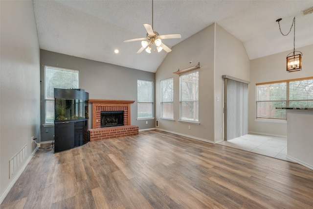 unfurnished living room with lofted ceiling, a brick fireplace, light hardwood / wood-style flooring, a textured ceiling, and ceiling fan