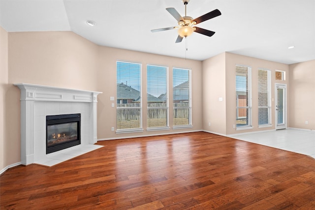 unfurnished living room featuring lofted ceiling, ceiling fan, light hardwood / wood-style floors, and a tiled fireplace