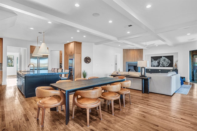 dining room featuring coffered ceiling, sink, light hardwood / wood-style flooring, a large fireplace, and beamed ceiling