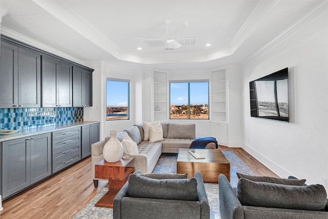 living room featuring built in features, ornamental molding, a raised ceiling, and light hardwood / wood-style flooring