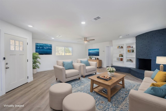 living room featuring a brick fireplace, built in features, ceiling fan, and light wood-type flooring