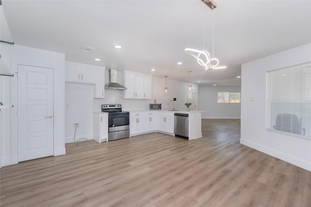 kitchen with appliances with stainless steel finishes, decorative light fixtures, white cabinets, and wall chimney exhaust hood