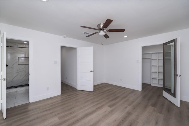 unfurnished bedroom featuring a walk in closet, ensuite bath, dark hardwood / wood-style floors, a closet, and ceiling fan