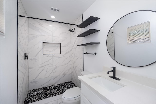 bathroom with a tile shower, vanity, and toilet