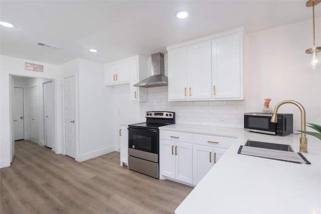 kitchen with stainless steel electric range, pendant lighting, white cabinets, wall chimney range hood, and light hardwood / wood-style flooring