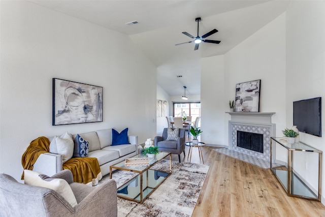 living room featuring high vaulted ceiling, light hardwood / wood-style floors, a premium fireplace, and ceiling fan