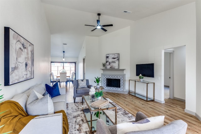 living room featuring ceiling fan, a fireplace, high vaulted ceiling, and light hardwood / wood-style flooring