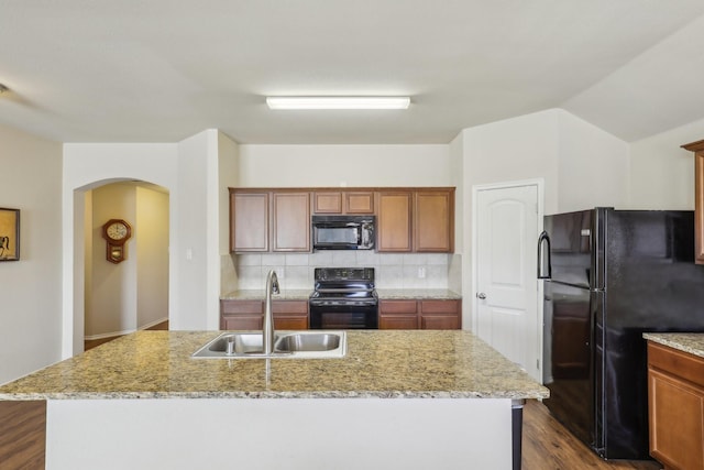 kitchen featuring light stone countertops, sink, a center island with sink, and black appliances