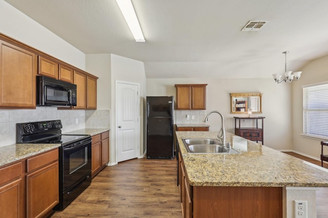 kitchen with pendant lighting, sink, black appliances, dark wood-type flooring, and a center island with sink