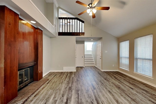 unfurnished living room featuring ceiling fan, wood-type flooring, high vaulted ceiling, and a brick fireplace