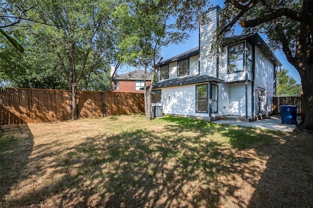 rear view of property featuring central AC unit and a lawn