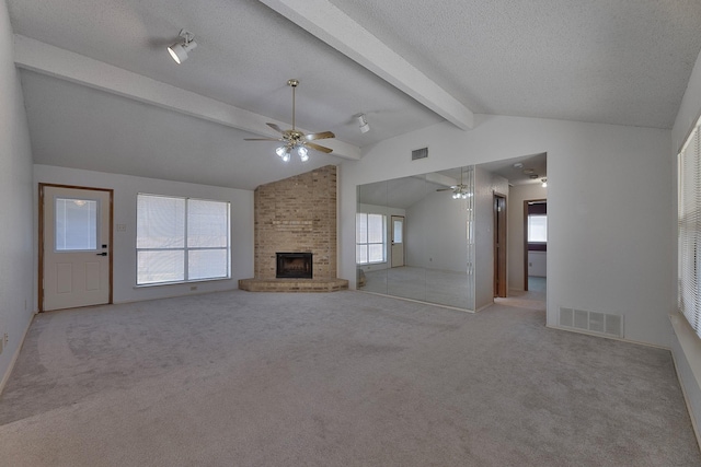 unfurnished living room featuring ceiling fan, a fireplace, lofted ceiling with beams, a textured ceiling, and light carpet