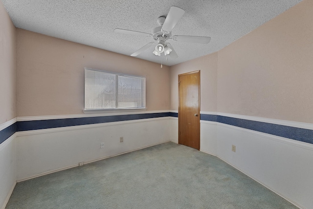 empty room featuring ceiling fan, light colored carpet, and a textured ceiling