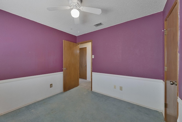 spare room featuring ceiling fan, light colored carpet, and a textured ceiling