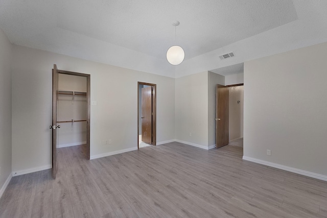 unfurnished bedroom featuring a walk in closet, light hardwood / wood-style floors, and a textured ceiling