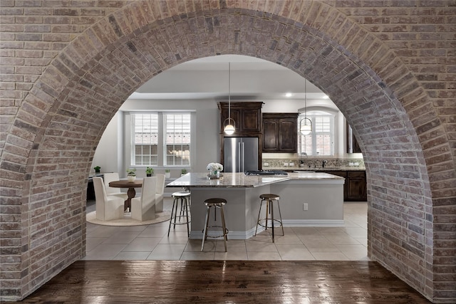 kitchen with a kitchen island, appliances with stainless steel finishes, light tile patterned floors, light stone countertops, and dark brown cabinets