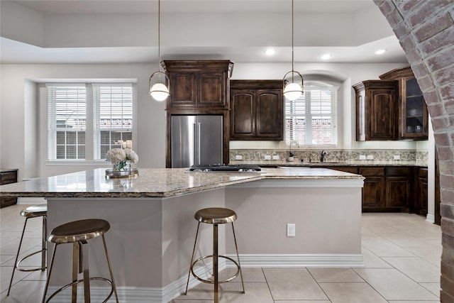 kitchen featuring dark brown cabinetry, decorative light fixtures, appliances with stainless steel finishes, a kitchen island, and light stone countertops