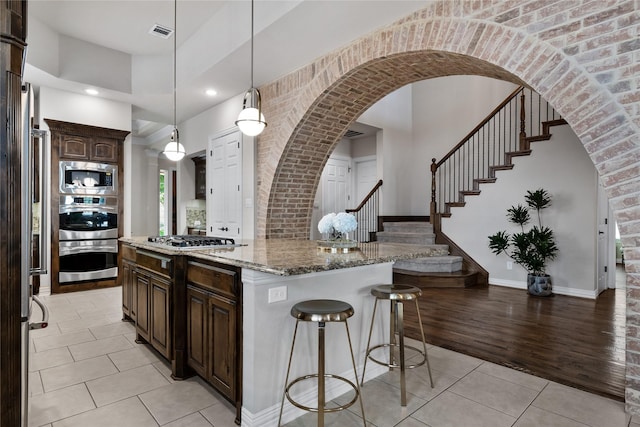 kitchen with hanging light fixtures, dark brown cabinets, stainless steel appliances, light stone counters, and a kitchen island