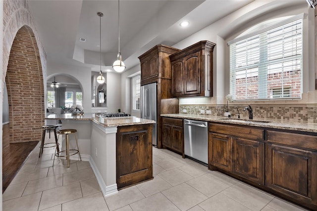 kitchen with sink, appliances with stainless steel finishes, light stone countertops, a kitchen island, and decorative light fixtures