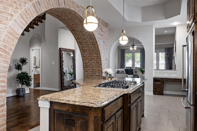 kitchen featuring light stone counters, decorative light fixtures, stainless steel appliances, and dark brown cabinetry