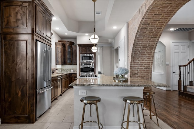 kitchen featuring stone counters, appliances with stainless steel finishes, pendant lighting, a center island, and dark brown cabinets