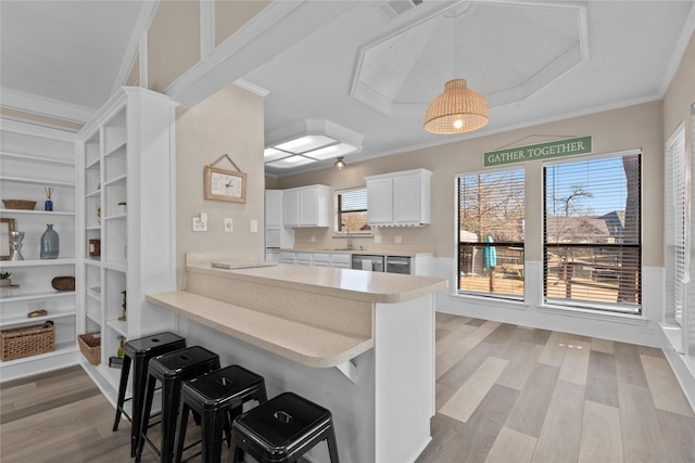 kitchen featuring a breakfast bar area, white cabinetry, crown molding, kitchen peninsula, and light hardwood / wood-style floors