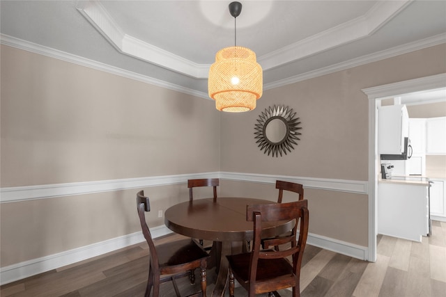 dining room featuring crown molding, a raised ceiling, and light hardwood / wood-style floors