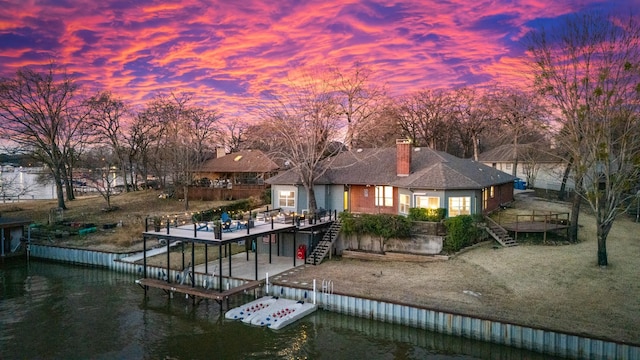 back house at dusk with a deck with water view and a yard