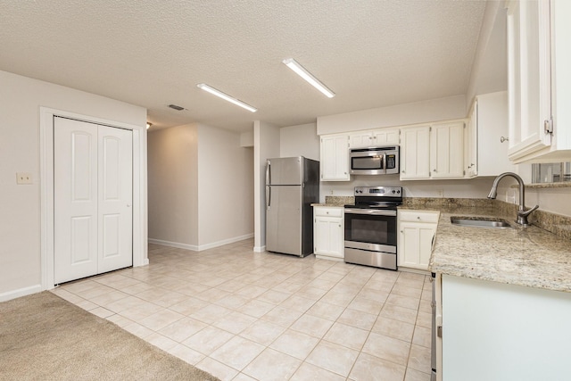 kitchen featuring sink, light tile patterned floors, appliances with stainless steel finishes, white cabinetry, and a textured ceiling