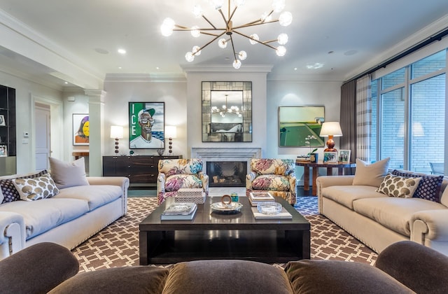 living room featuring crown molding, a notable chandelier, a fireplace, and ornate columns