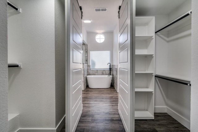 walk in closet featuring dark wood-type flooring, visible vents, and a barn door