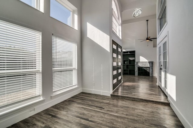 foyer featuring a towering ceiling, ceiling fan, a fireplace, and dark wood-type flooring