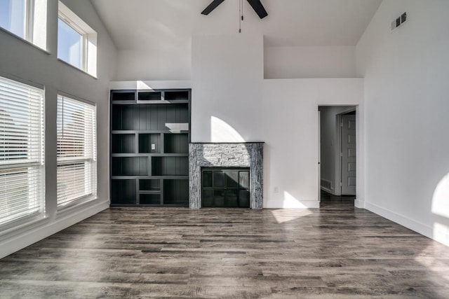 unfurnished living room with visible vents, a towering ceiling, dark wood-type flooring, a glass covered fireplace, and a ceiling fan