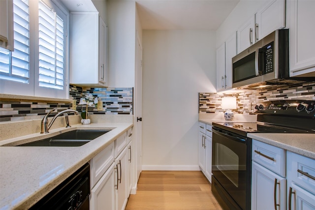 kitchen with sink, white cabinetry, light stone counters, black appliances, and light wood-type flooring