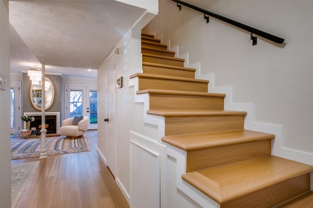 staircase featuring wood-type flooring, french doors, and a textured ceiling