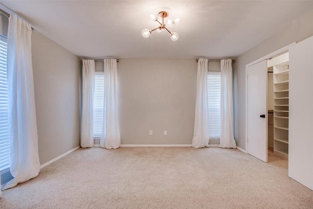 empty room with a notable chandelier, a wealth of natural light, and light colored carpet