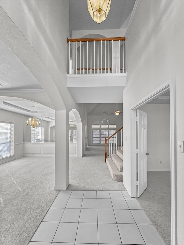 foyer entrance with crown molding, ceiling fan with notable chandelier, light carpet, and a high ceiling