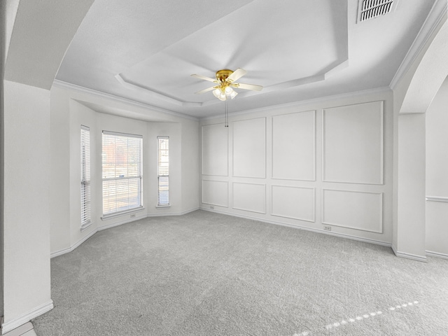 carpeted spare room with a raised ceiling, crown molding, and ceiling fan