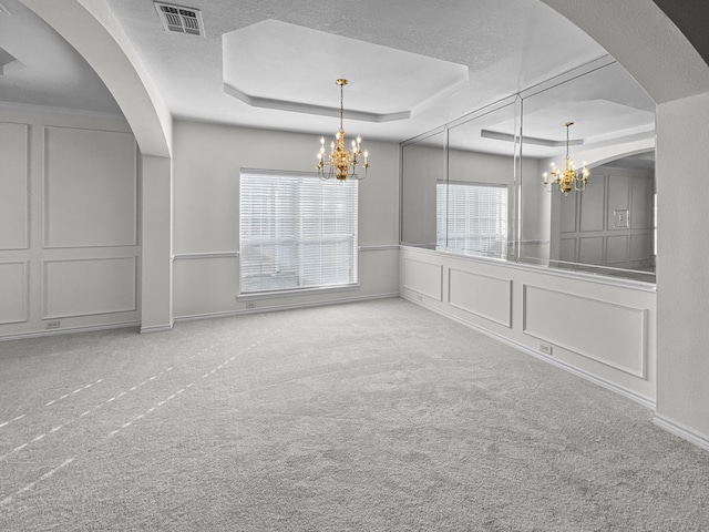 unfurnished dining area with a tray ceiling, light carpet, and a notable chandelier