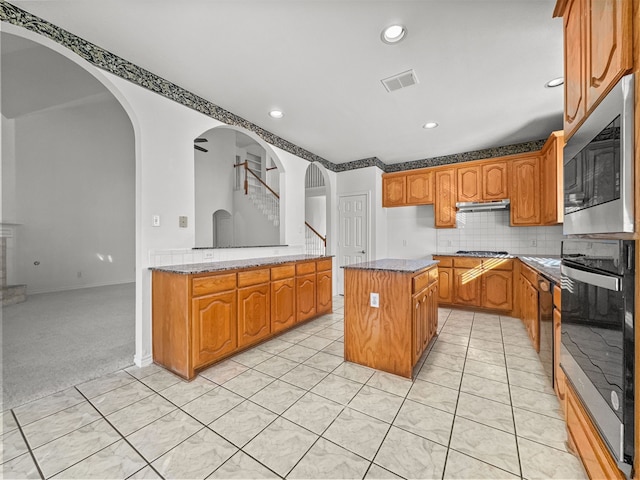 kitchen with light tile patterned flooring, tasteful backsplash, light stone counters, a center island, and stainless steel appliances