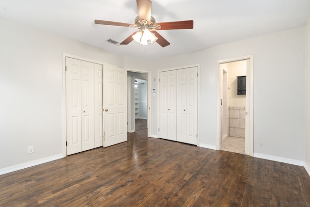 unfurnished bedroom with ceiling fan, ensuite bathroom, dark hardwood / wood-style floors, and two closets