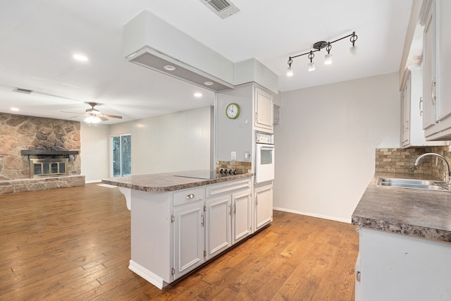 kitchen with sink, black electric stovetop, a fireplace, white cabinets, and oven