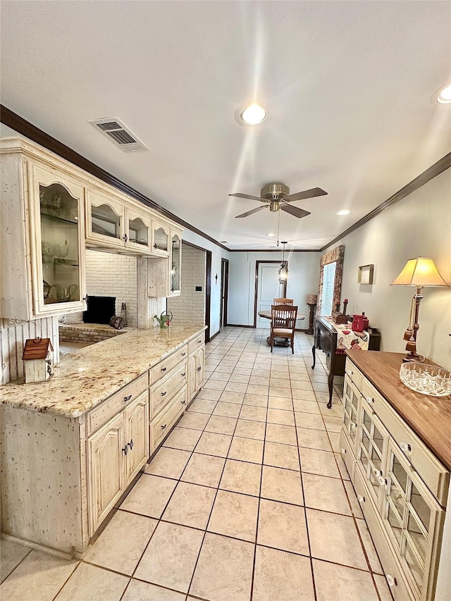 kitchen featuring light tile patterned floors, visible vents, ceiling fan, glass insert cabinets, and ornamental molding