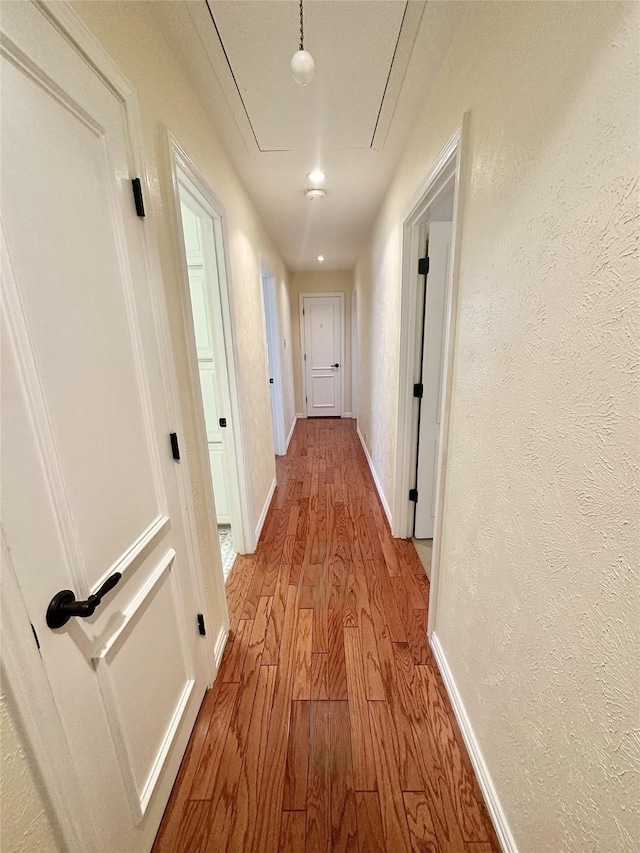 hall featuring a textured wall, wood finished floors, attic access, and baseboards