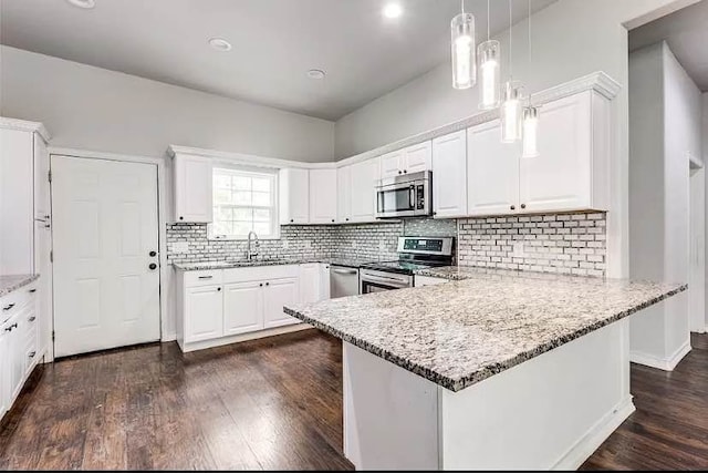 kitchen with appliances with stainless steel finishes, pendant lighting, white cabinets, light stone counters, and kitchen peninsula