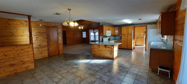 kitchen featuring pendant lighting, sink, a chandelier, a kitchen bar, and kitchen peninsula