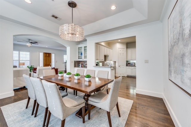 dining space featuring crown molding, a tray ceiling, dark hardwood / wood-style flooring, and ceiling fan with notable chandelier