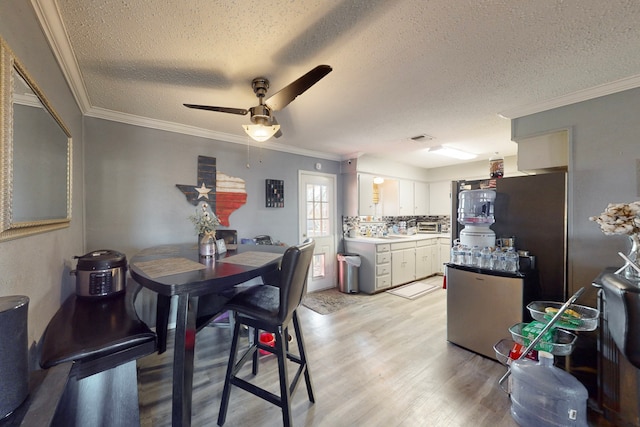 dining room with crown molding, ceiling fan, a textured ceiling, and light wood-type flooring