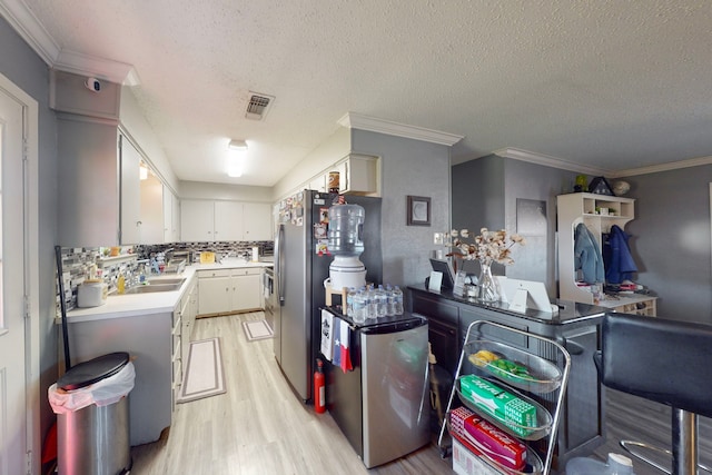 kitchen with light hardwood / wood-style flooring, crown molding, stainless steel fridge, and tasteful backsplash