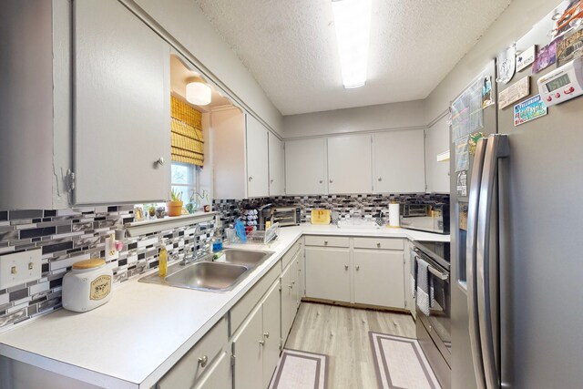 kitchen with sink, light hardwood / wood-style flooring, appliances with stainless steel finishes, tasteful backsplash, and a textured ceiling